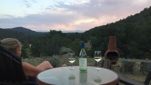 Una persona sentada a una mesa redonda al aire libre, con una botella y dos copas de vino blanco.