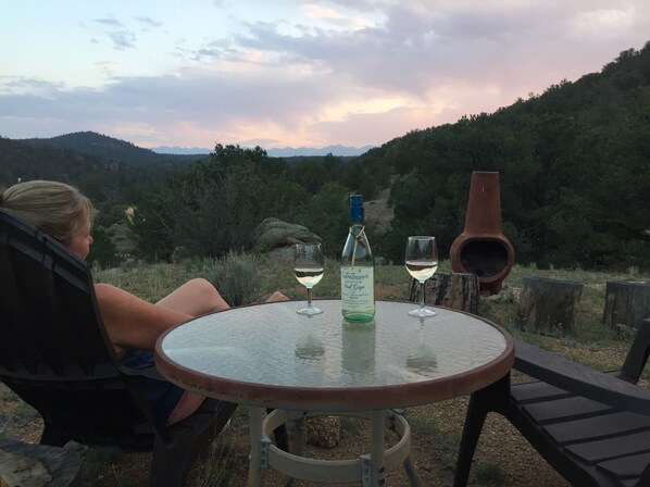A person seated at a round table outdoors with a bottle and two glasses of white wine. - Big Tiny Home w/ Huge Deck w/ amazing views of the Sangre Mountains (Off-Grid) (Cotopaxi)