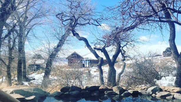 Un estanque transparente rodeado de rocas y árboles, con una casa al fondo.