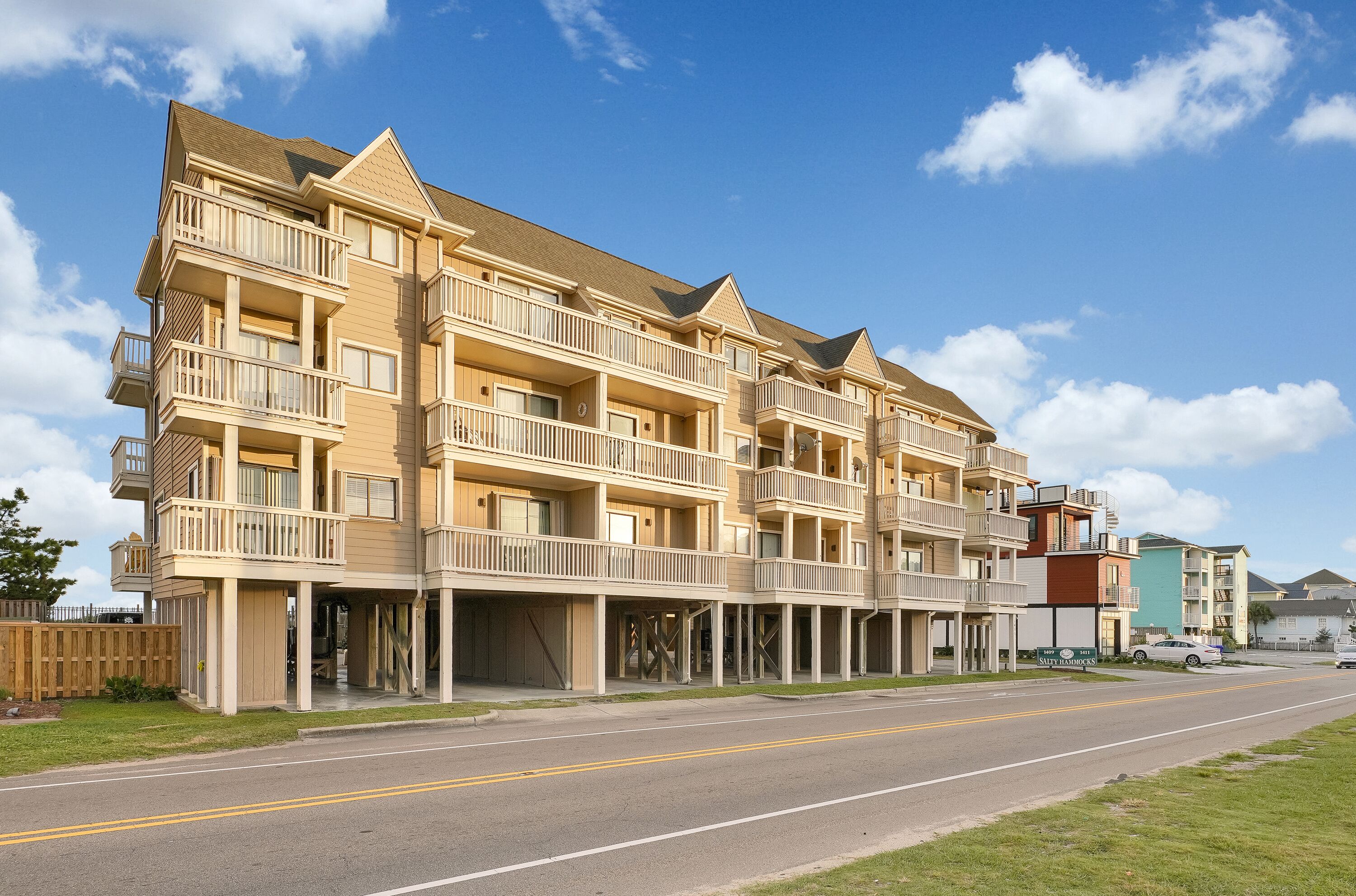 Um edifício residencial com vários andares, varandas, uma rua em frente e céu aberto.