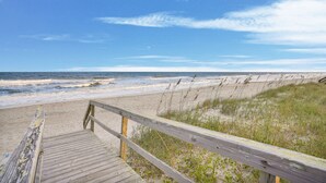 Une promenade en bois qui mène à une plage de sable où l’on peut admirer les vagues de l’océan.