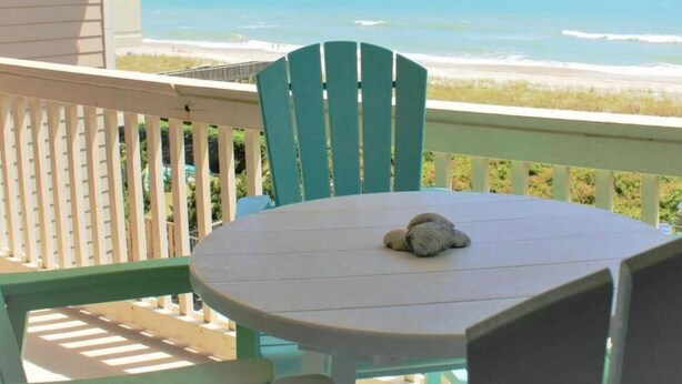 Un balcon avec vue sur l’océan, une table ronde et une seule chaise.