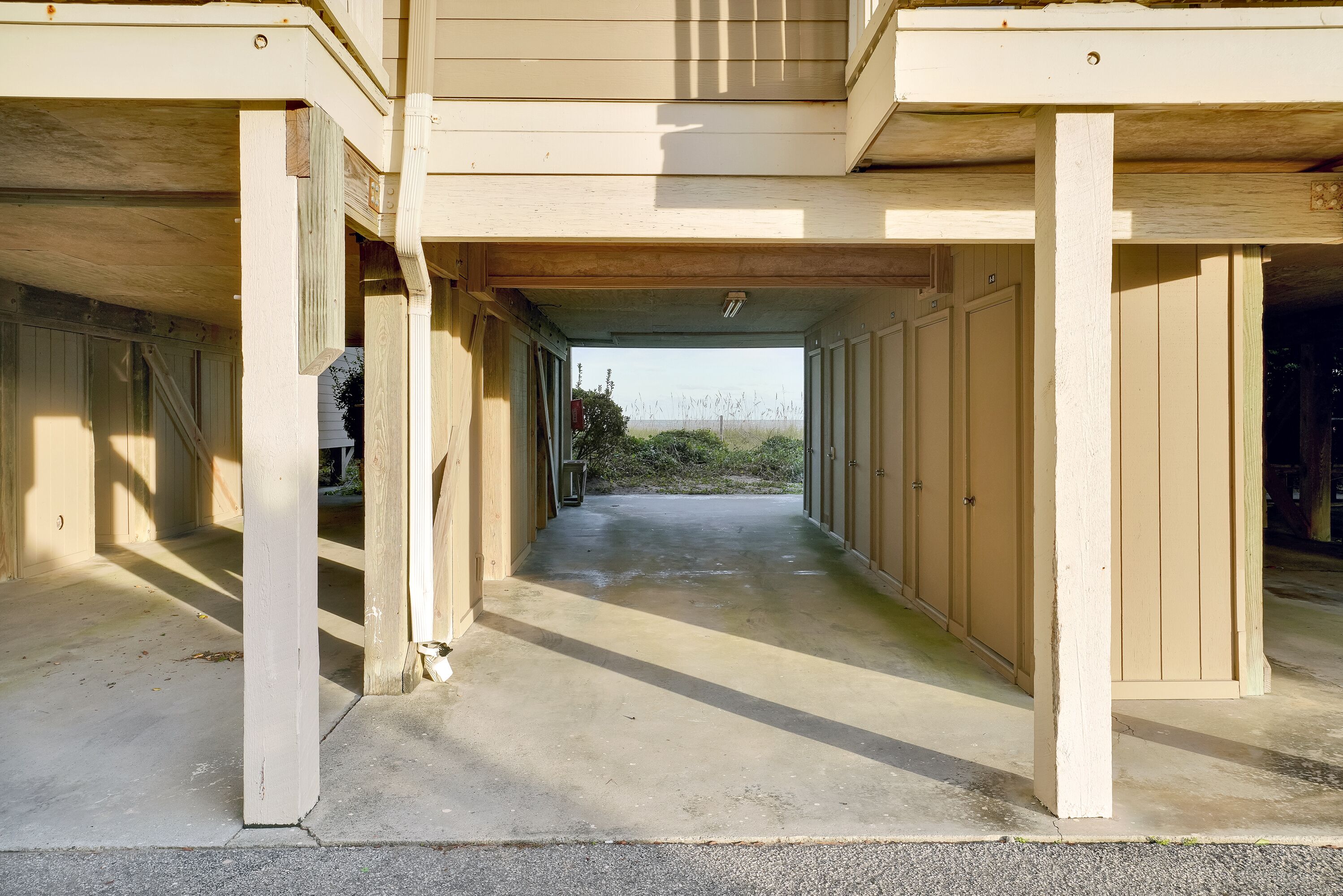 Ein überdachter Außenbereich mit Betonboden und Holzsäulen, der zu einer Garage mit mehreren Einfahrten führt.