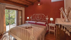 A bedroom with a wooden ceiling, a bed with a white headboard, two bedside tables with lamps, a nightstand, and a decorative vase with sticks. - Beautiful home in Giarratana (Giarratana)
