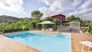 A swimming pool with a patio area, a covered seating area, and a view of a red house in the background. - Beautiful home in Giarratana (Giarratana)