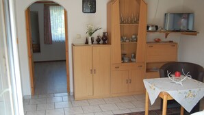 Una habitación con un armario de madera, una mesa con mantel, una silla y un televisor sobre una estantería.