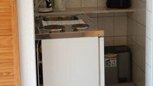 Una kitchenette compacta con un lavamanos, un refrigerador pequeño, una cafetera y un basurero.