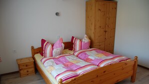 Una cama de madera con colcha y almohadas a rayas, una mesita de noche de madera y un armario de madera en una habitación con paredes de color claro y suelo de madera.