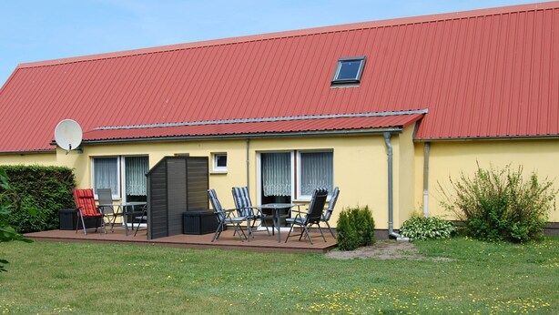 Un edificio amarillo con techo rojo, una antena parabólica y un patio con mobiliario exterior.