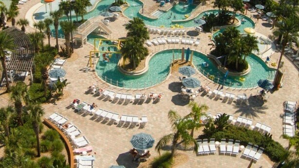 An aerial view of a resort with multiple swimming pools, sun loungers, and palm trees.