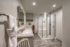 A bathroom with a glass-enclosed shower, a marble sink, and a towel rack.