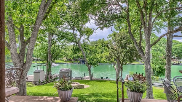 A deck with outdoor seating, a grassy area, and a view of a lake with boats. - LD 727 Down River Haus (New Braunfels)