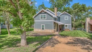 A two-story house with a stone chimney, a front porch, and a well-maintained lawn. - LD 727 Down River Haus (New Braunfels)