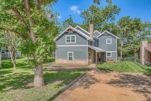 A two-story house with a stone chimney, a front porch, and a well-maintained lawn. - LD 727 Down River Haus (New Braunfels)