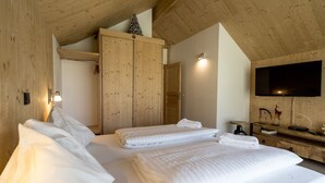 Quarto com duas camas, guarda-roupa de madeira, televisão e uma pequena mesa com objetos decorativos.