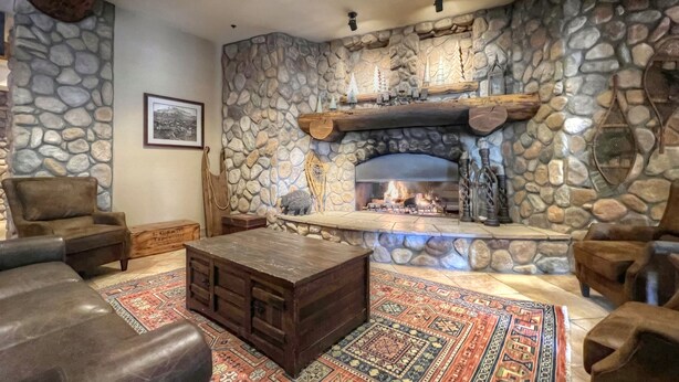 Une cheminée en pierre avec un feu, entourée de canapés en cuir et d’un tapis à motifs.