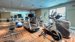 Une salle de sport équipée de tapis de course, de vélos elliptiques et de ballons d’exercice.