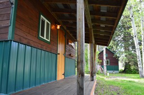 A wooden cabin with a porch, green trim, and a window.