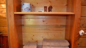 A wooden cabinet with a shelf containing a roll of toilet paper, two small tubes, and a stack of folded towels. - Last minute Plan to Glacier Guest Cabin Sauna  (Essex)