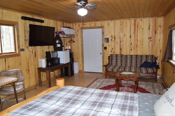 A wooden-paneled room with a bed, a sofa, a television, and a coffee maker.