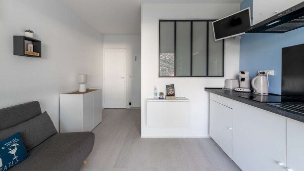 Una cocina moderna con armarios blancos, encimera negra y televisor integrado.
