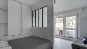Un dormitorio con cama, armario, ventana y balcón.