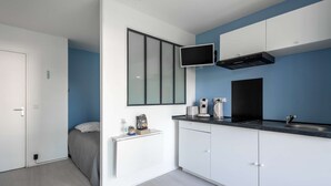 Cocina compacta con gabinetes blancos, encimera negra, microondas integrado y campana extractora negra.