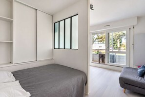 A bedroom with a bed, a grey sofa, a window, and a door leading to an outdoor area.