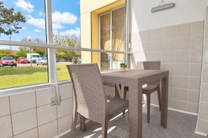 A balcony with wicker furniture, a view of parked cars, and a sign indicating 'Plage 200 M'.