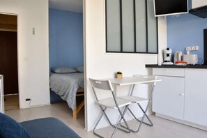 A compact room with a bed, a foldable table, a chair, a TV, and a kitchenette.