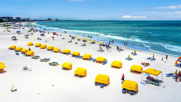 Ein Strand mit Reihen aus gelben Sonnenschirmen und blauen Liegestühlen.