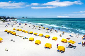 A beach with rows of yellow umbrellas and blue lounge chairs.