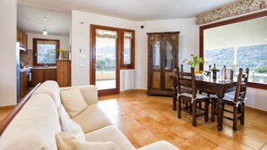 A living room with a sofa, dining table, chairs, and a view through a large window. - Luxury Villa Laura - new infinity pool, relax and privacy for your holidays (Alghero)