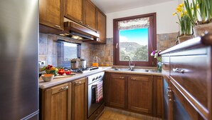 A kitchen with wooden cabinets, a stove, a sink, and a window with a view of the outdoors. - Luxury Villa Laura - new infinity pool, relax and privacy for your holidays (Alghero)