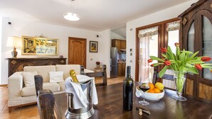 A living room with a sofa, a dining table with a bottle of wine, a bowl of fruit, and a vase of tulips. - Luxury Villa Laura - new infinity pool, relax and privacy for your holidays (Alghero)