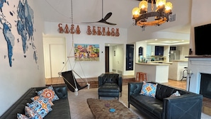 A spacious living area with leather sofas, a hanging chair, and a fireplace. A kitchen is visible in the background. - Palm Springs Private Retreat Pool & Mountain Views (Palm Springs)