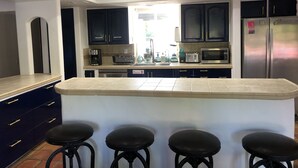 A kitchen with dark cabinets, a central island with stools, a refrigerator, and a coffee maker. - Palm Springs Private Retreat Pool & Mountain Views (Palm Springs)