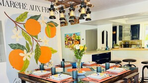 A dining area with a wooden table set for six, a hanging light fixture, and a mural with fruit and flowers. - Palm Springs Private Retreat Pool & Mountain Views (Palm Springs)