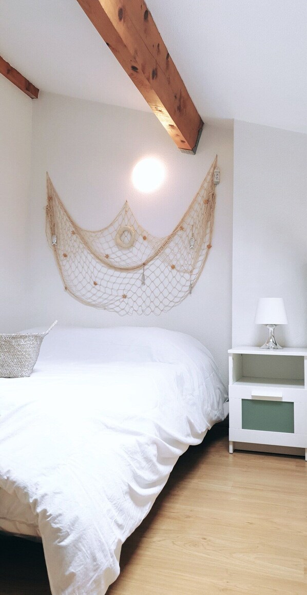 A bedroom with a bed, a bedside table, a wall hanging, and a wooden ceiling beam.