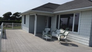 Een gelijkvloers huis met een overdekte veranda, een witte hek en een rij van drie rieten stoelen.