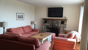 Een woonkamer met een stenen openhaard, een televisie erboven en een zithoek.