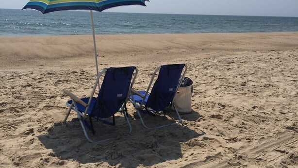 Een strand met twee blauwe strandstoelen en een gestreepte parasol.