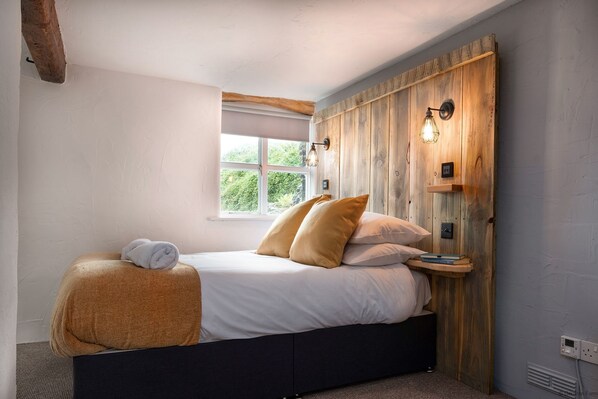 A bedroom with a bed, pillows, a bedside table, a window, and a wooden headboard. - The Granary - sleeps 2 guests in 1 bedroom (Bryncrug)