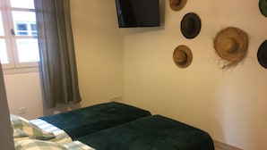 A room with two beds, a television mounted on the wall, and several hats displayed on the wall.