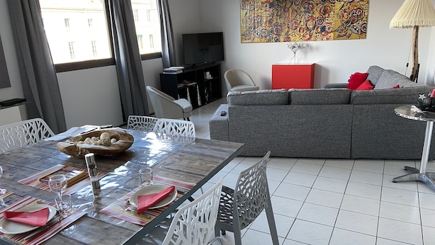 A modern living room with a dining area, grey sofa, and a colorful abstract painting on the wall.