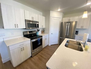 Una cocina moderna con armarios blancos, electrodomésticos de acero inoxidable, un horno negro y un lavamanos grande.