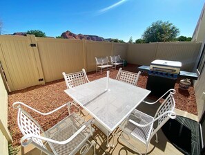 An outdoor patio with a white metal table and chairs, a barbecue grill, and a fenced area with a view of red rock formations. - Modern 3BR Townhome Near Zion & Bryce | Sleeps 8 (Kanab)