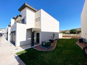 A modern two-story residential building with a flat roof, a covered outdoor area, and a well-maintained lawn. - Modern 3BR Townhome Near Zion & Bryce | Sleeps 8 (Kanab)