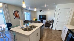 Una cocina moderna con una isla central, un comedor con sillas, un televisor y un ventilador de techo.