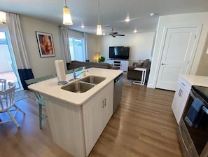 Una cocina moderna con una isla central, un comedor con sillas, un televisor y un ventilador de techo.